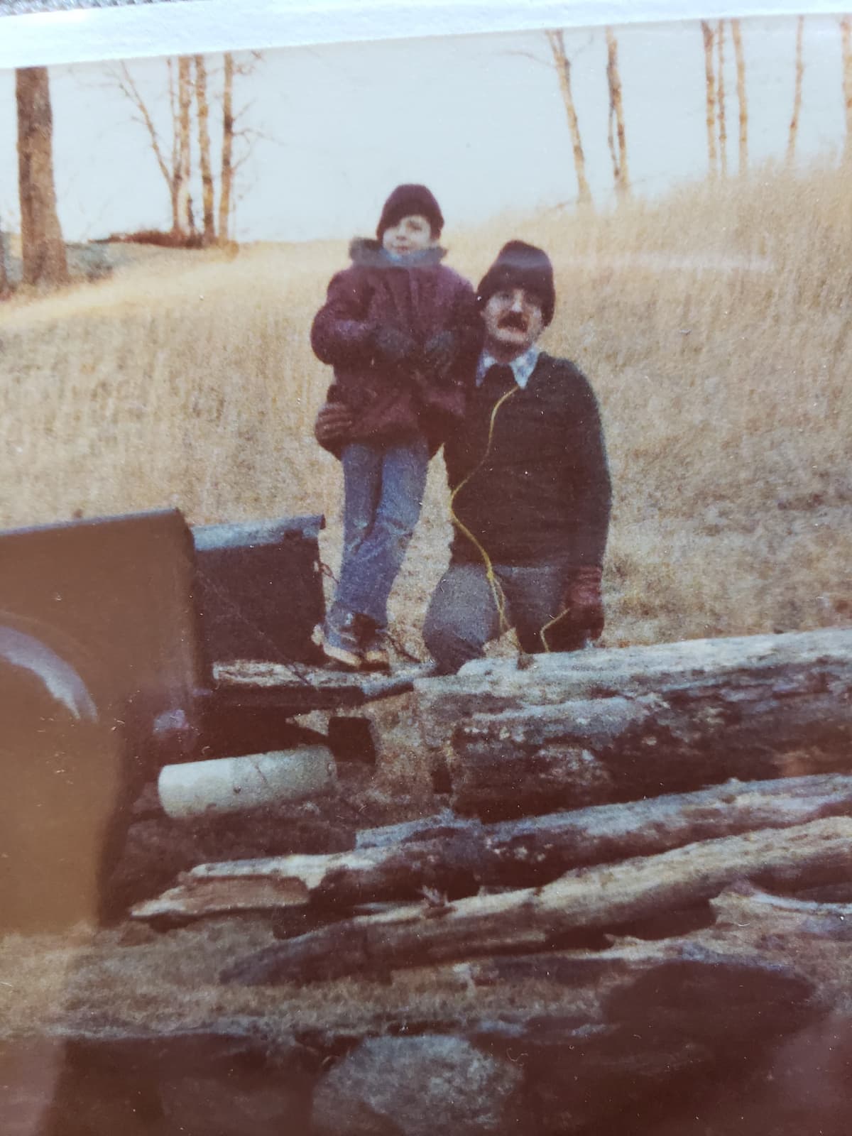 Chris as a child with his father, standing on a truck bed full of freshly cut logs in rural Connecticut